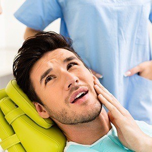 Man in dental chair holding cheek before root canal therapy