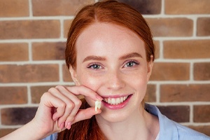 A young female with red hair smiling and holding an extracted tooth next to her mouth