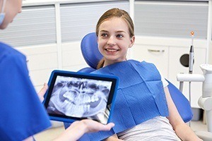 Dentist examining digital x-rays of young girl smiling in dental chair