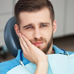 Man in dental chair holding cheek before emergency dentistry