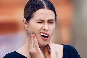 Woman holding cheek in pain before wisdom tooth extractions