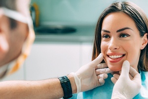 A dentist visually examining a female patient’s smile and facial structure for signs of oral cancer