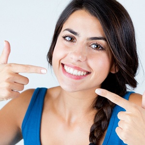 Woman pointing to smile after all porcelain dental crown restoration