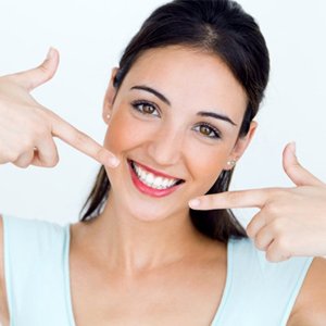 A woman with porcelain veneers pointing at her smile