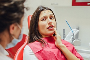 A female patient holding her cheek in pain while listening to her dentist explain the process of a root canal procedure