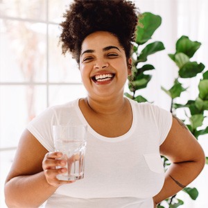 Smiling woman holding a glass of water near a bright window