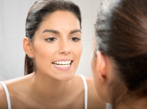 Woman looking at her brilliant smile in the mirror after teeth whitening in Lincoln