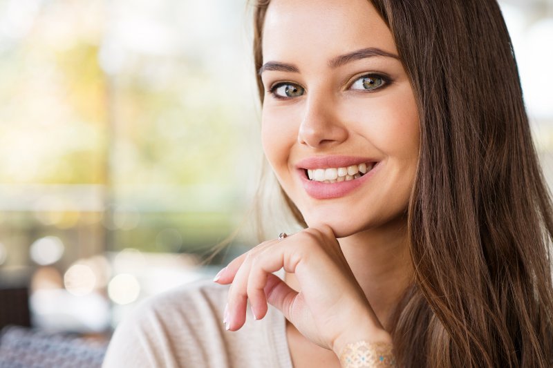 a young female with long, dark hair propping her chin on her hand and showing off her new and improved smile