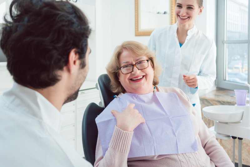 an older woman smiling while talking to her dentist and dental hygienist