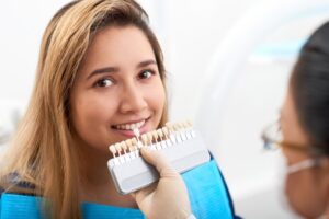 woman smiling with the dentist holding up a color guide to her mouth