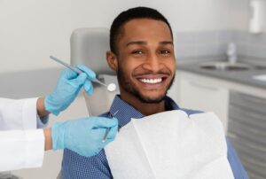 smiling male patient with the dentist’s hands and tools beside his face