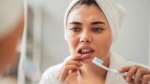 woman looking at her gums in the mirror with a toothbrush in her hand