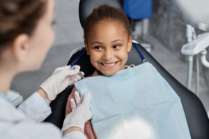 little girl with a huge smile with baby teeth in the dentist’s chair