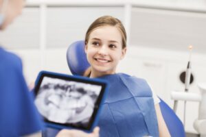 young girl smiling while dentist looks at X-rays
